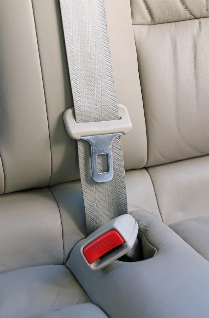 Light grey seat belt with latch tongue and press-release buckle on a cream leather rear bench seat