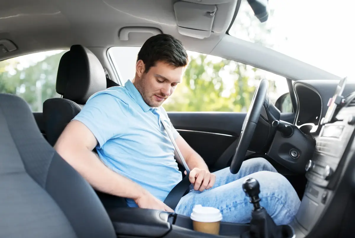 Driver in a blue polo shirt fastening a seat belt inside a vehicle cabin