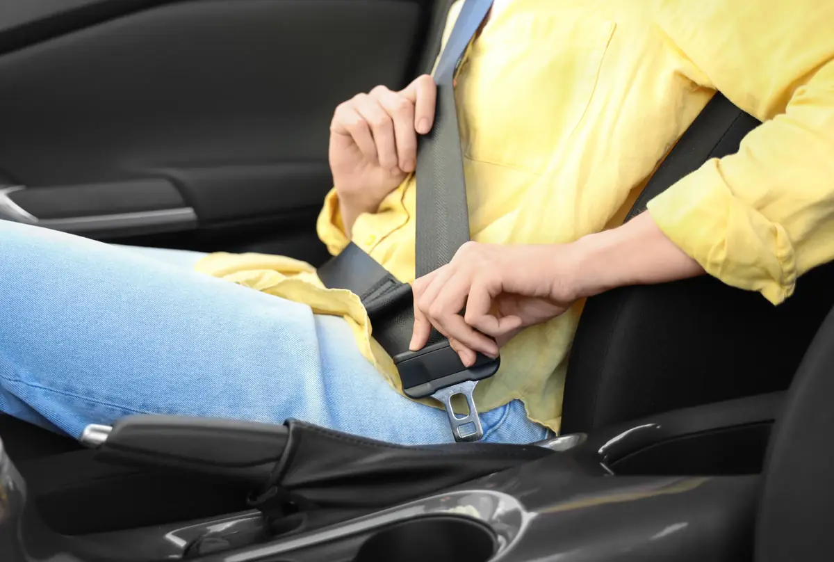 Person in a yellow shirt guiding a seat belt latch tongue towards the buckle inside a car