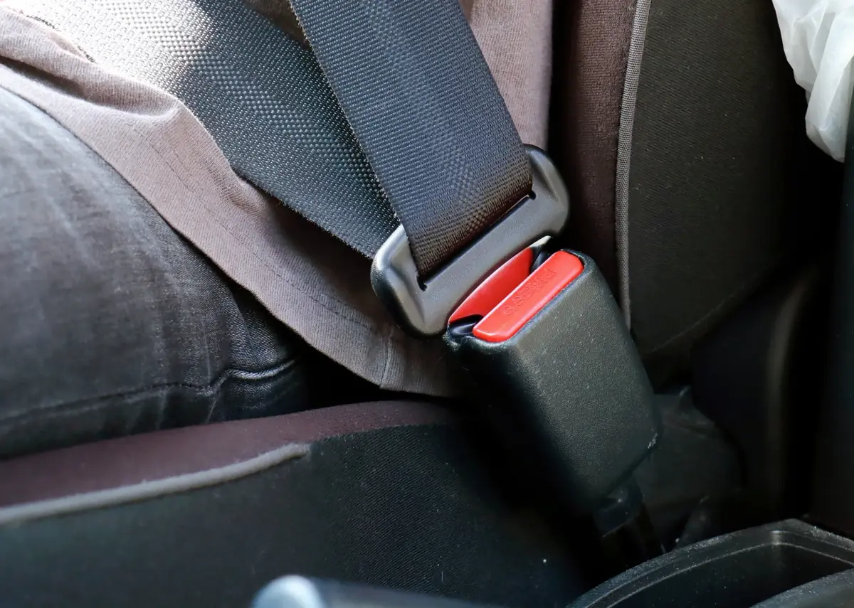 Seat belt buckle engaged beside a fabric vehicle seat with the webbing running up towards the pillar