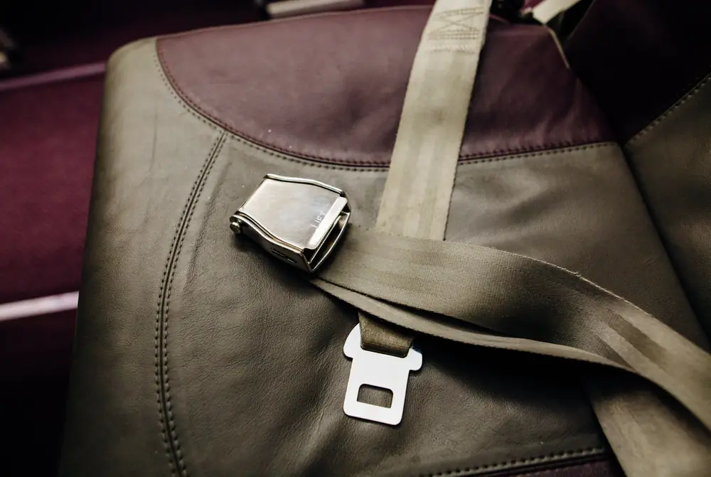 Lift-latch style metal seat belt buckle resting on a leather passenger seat