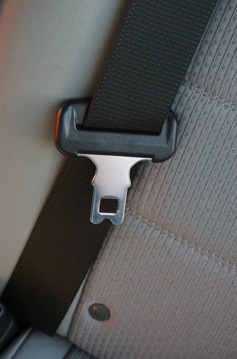 Chrome seat belt latch plate held in a moulded pillar loop against grey seat trim