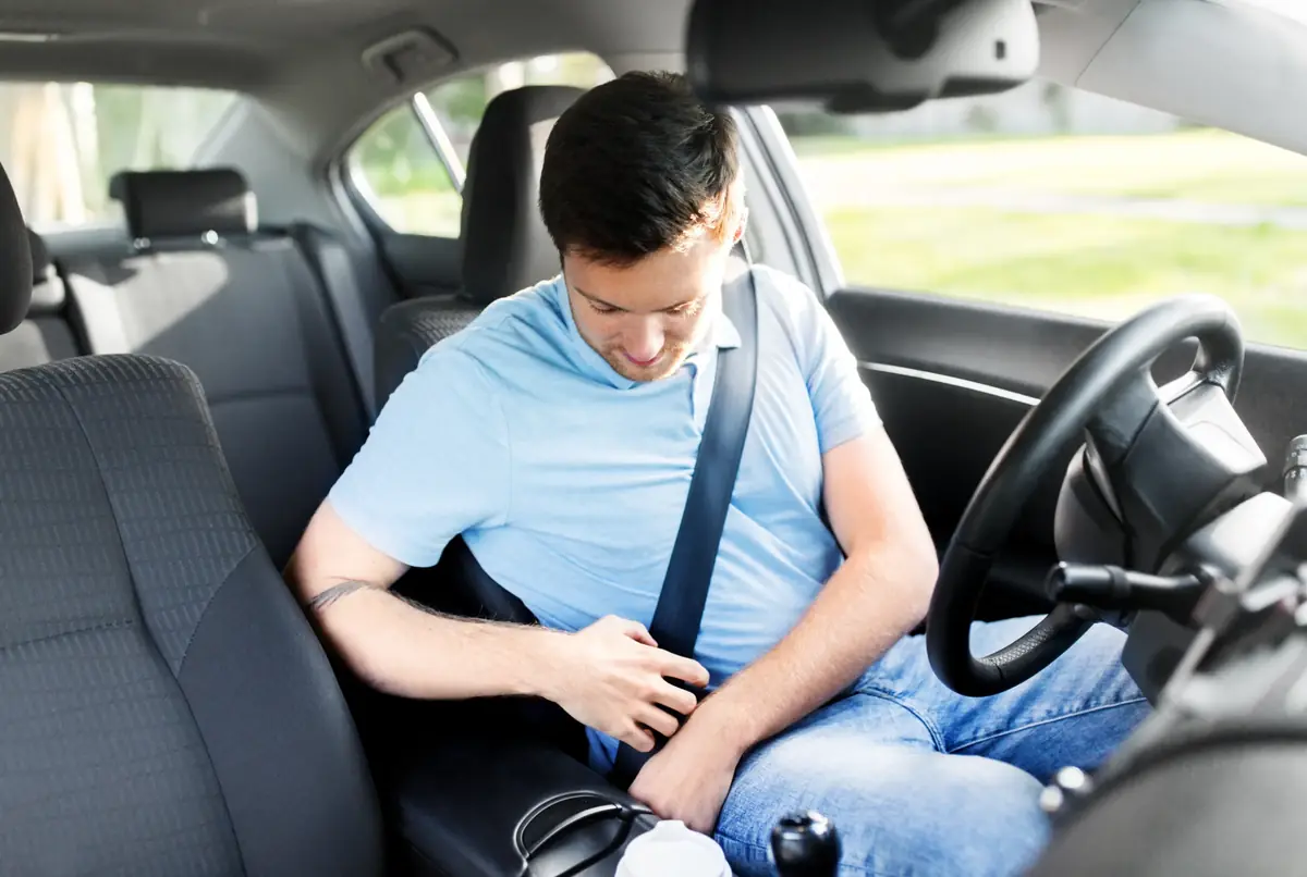 Driver in a light blue shirt fastening a three-point seat belt in the front seat of a car