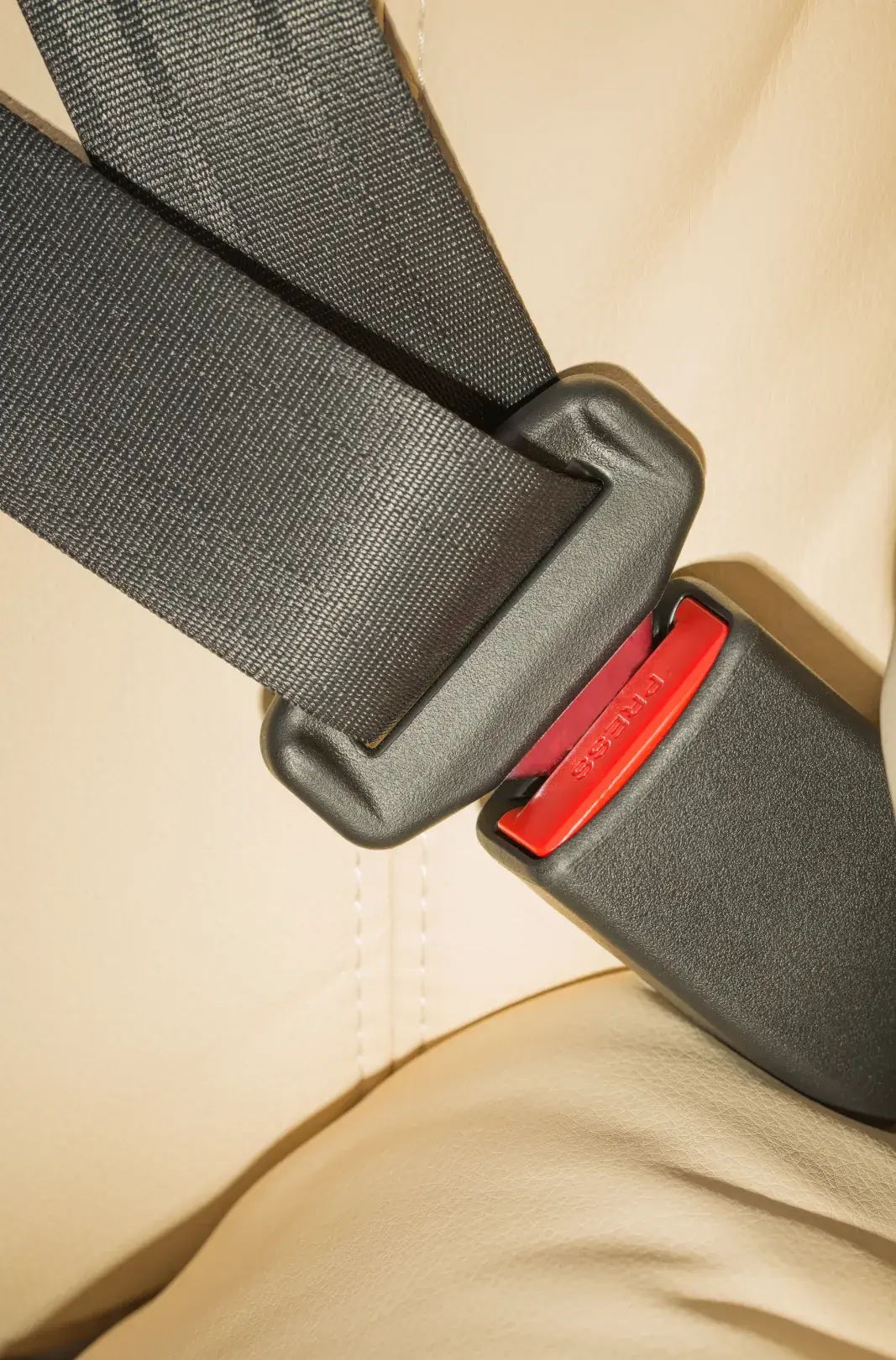 Dark seat belt webbing latched into its buckle across a cream leather vehicle seat