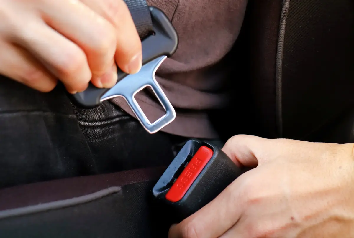 Two hands guiding a seat belt latch tongue into the buckle receptacle to verify clean engagement