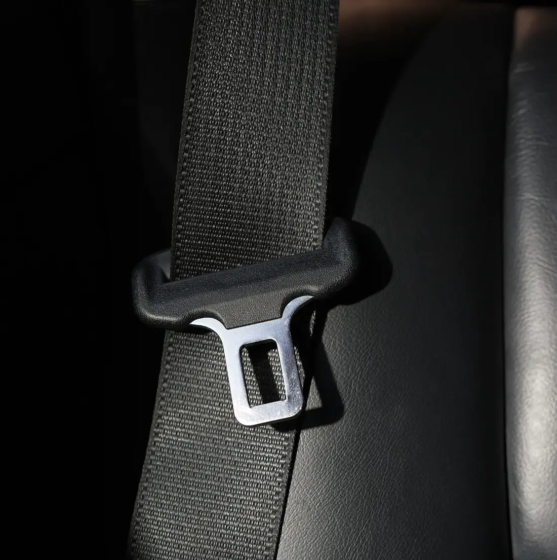 Seat belt webbing running through a moulded pillar loop, showing the weave and the edge of the strap